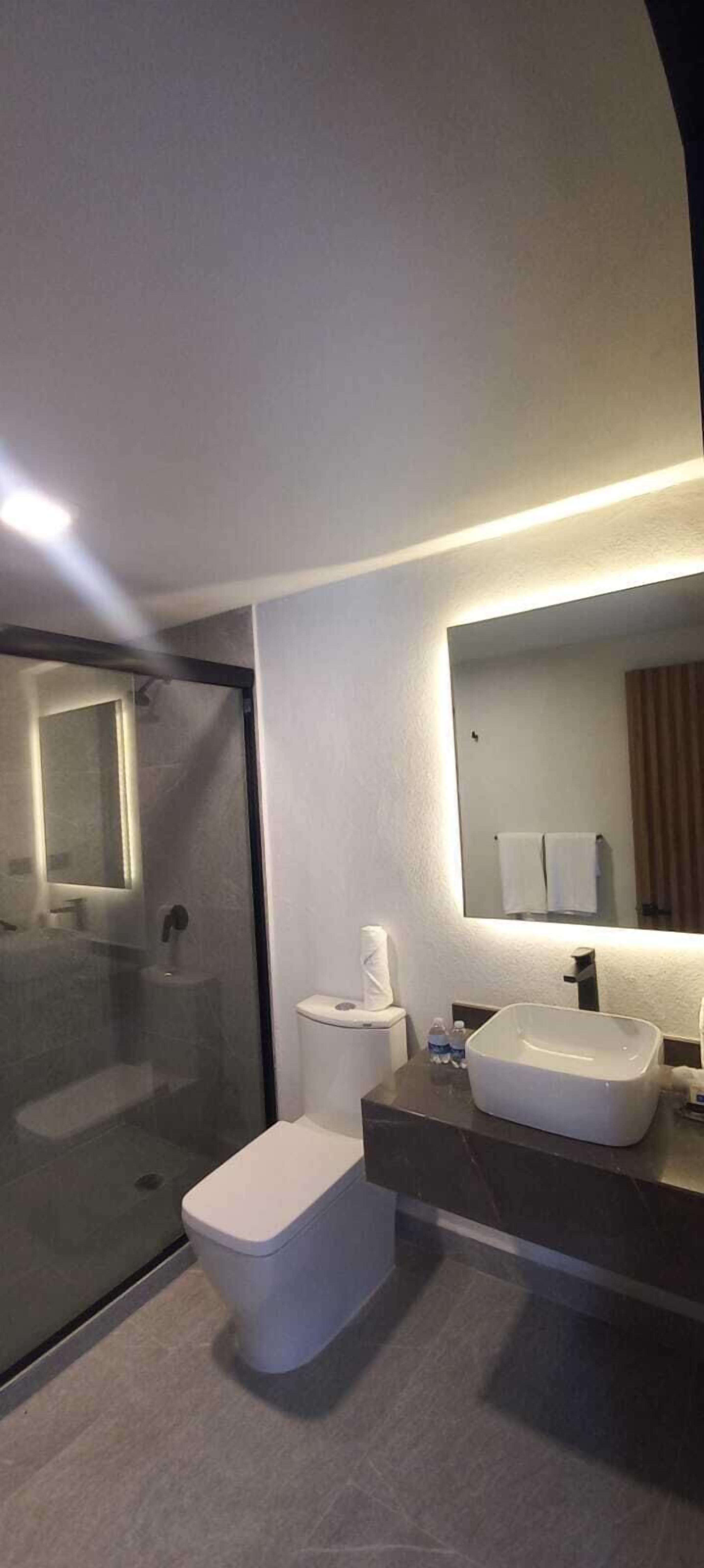 Un baño moderno con cabina de ducha de vidrio, inodoro, lavabo y espejo.