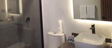 Un baño moderno con cabina de ducha de vidrio, inodoro, lavabo y espejo.