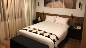 Habitación de hotel con una cama grande, una mesita de noche con un teléfono, una mesita de noche pequeña con una caja de pañuelos y una obra de arte colgada en la pared sobre la cama.