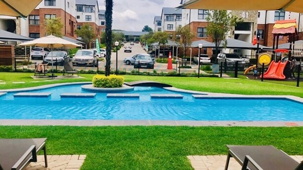 Ein Schwimmbecken mit einer kleinen Insel in der Mitte, umgeben von Rasen und Bänken.