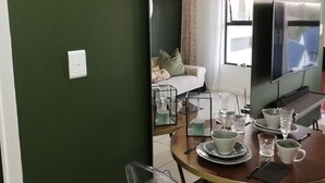 Ein Essbereich mit einem runden Tisch, gedeckt für vier Personen, einem großen Spiegel, der den Raum reflektiert, und einer Uhr an der Wand.