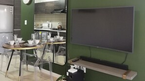 Eine moderne Küche mit grüner Wand, einem großen Spiegel, einem Flachbildfernseher und einem Essbereich mit klaren Stühlen und einem Tisch für zwei Personen.