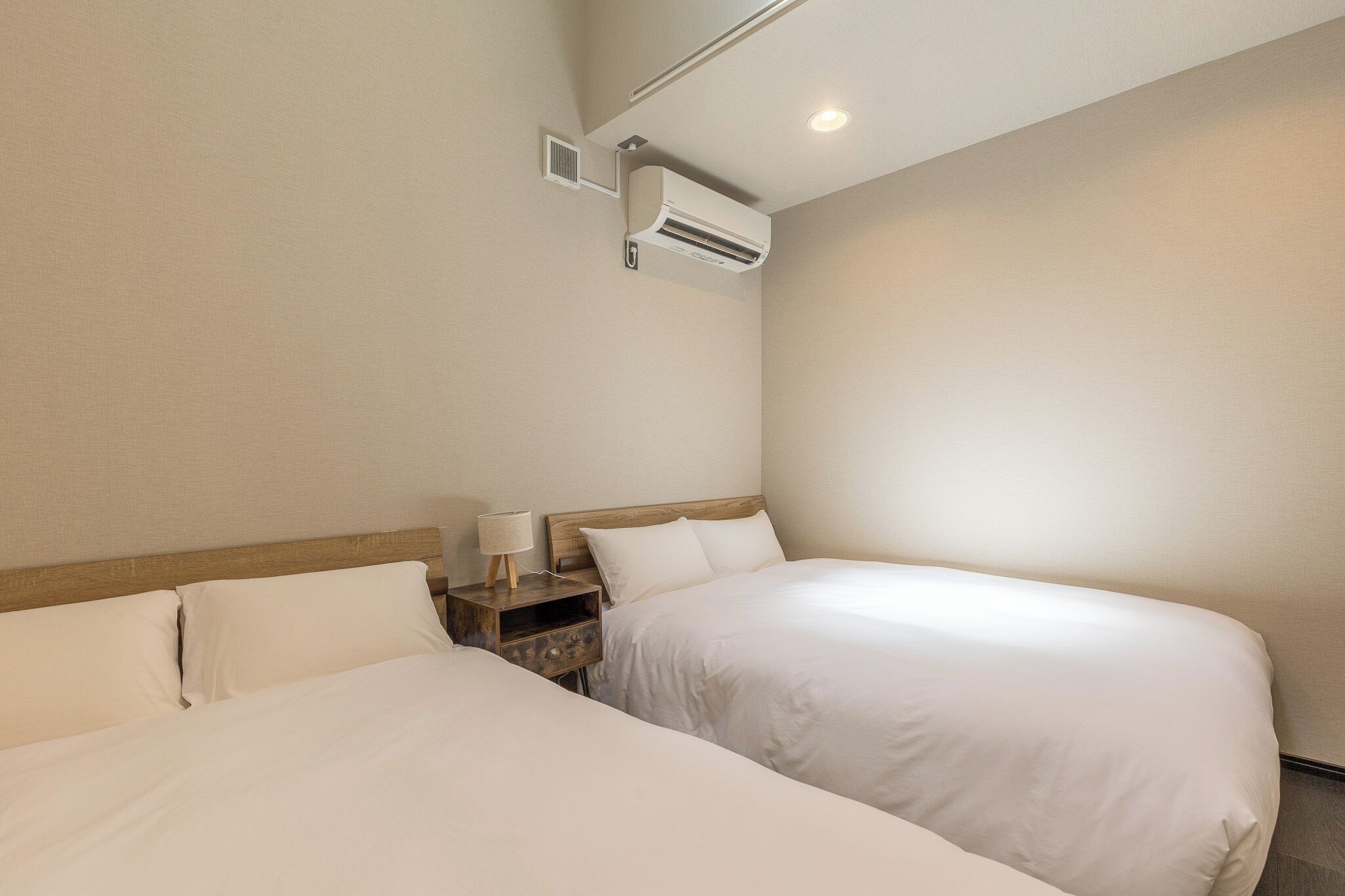 Une chambre d’hôtel avec deux lits, une table de chevet, une lampe et un appareil de climatisation.