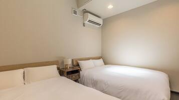 Une chambre d’hôtel avec deux lits, une table de chevet, une lampe et un appareil de climatisation.