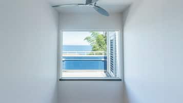 Una habitación con ventilador de techo, ventana con vista a un edificio azul y un árbol.