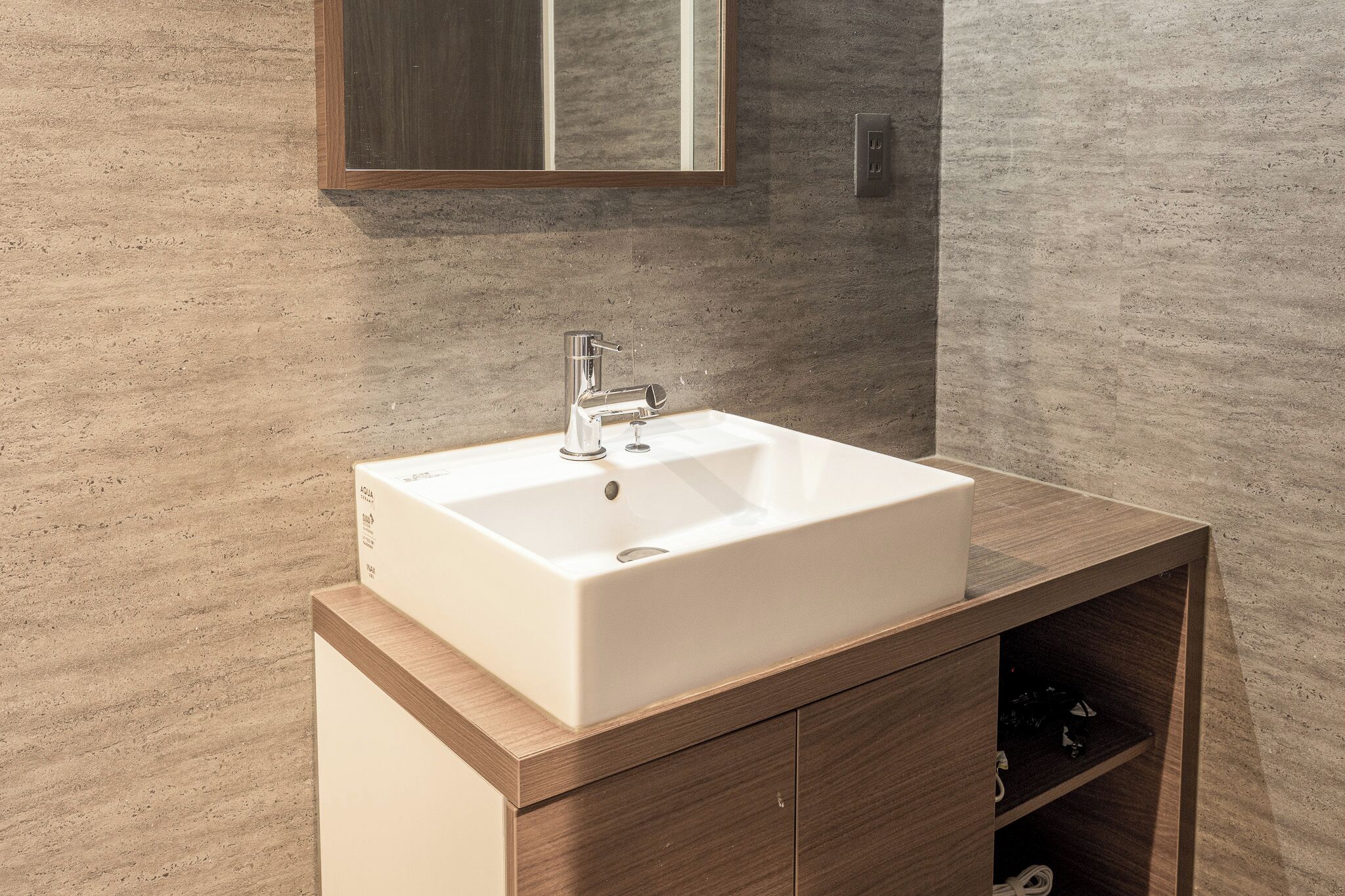 A bathroom with a white sink, wooden vanity, and a mirror above the sink.