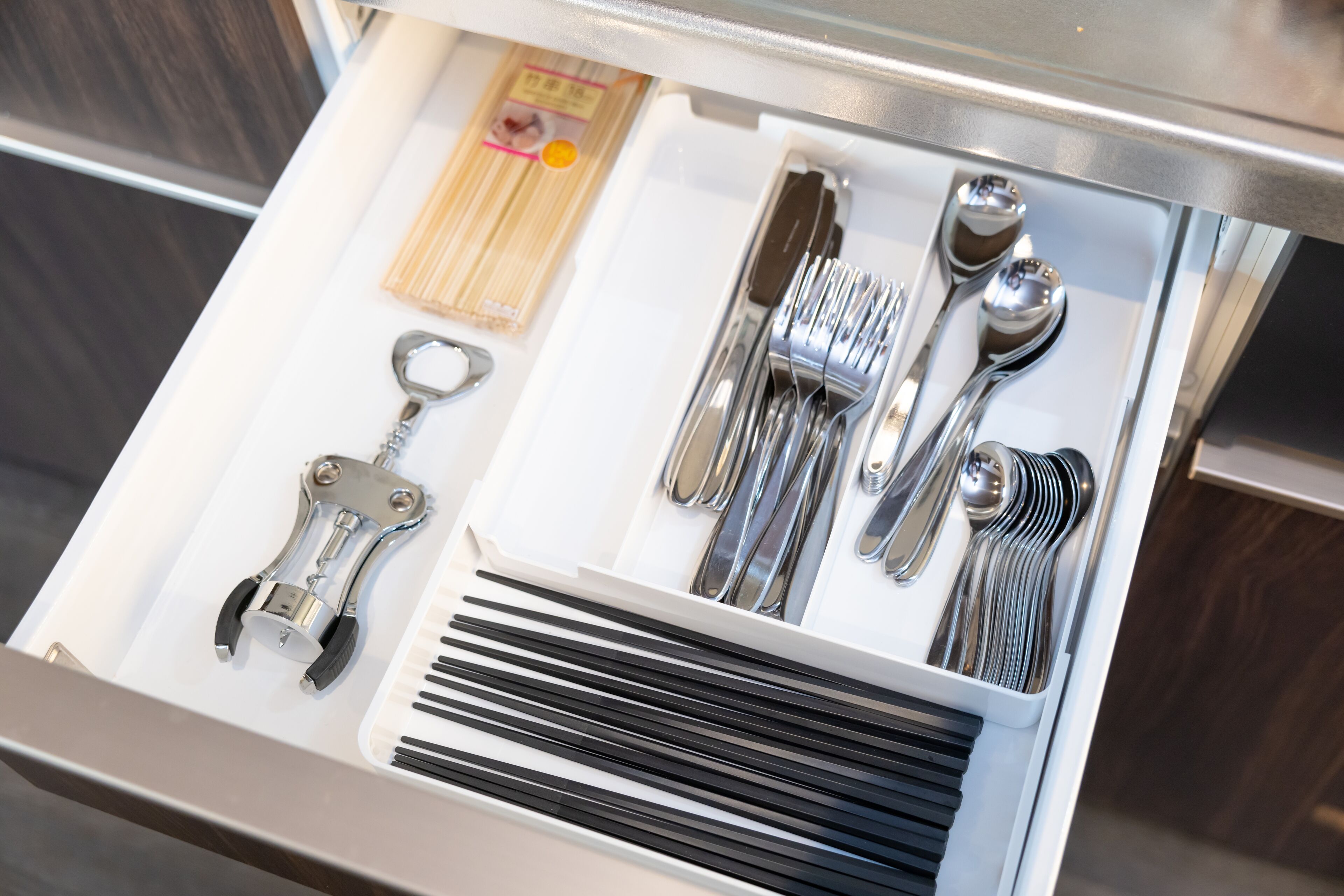 A drawer containing a set of silverware, including a fork, knife, spoon, and chopsticks.