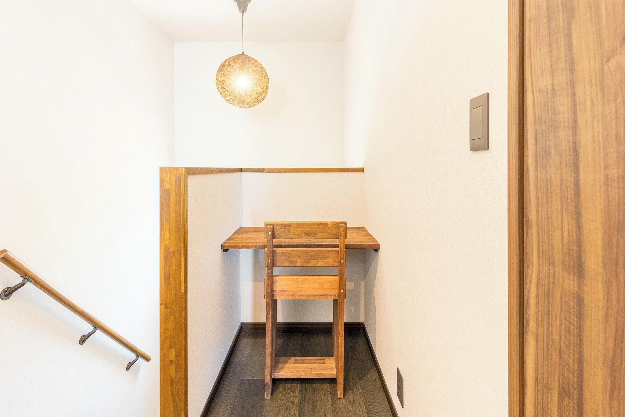 A narrow stairway with a wooden bench at the top, a handrail on the left, and a light fixture above.