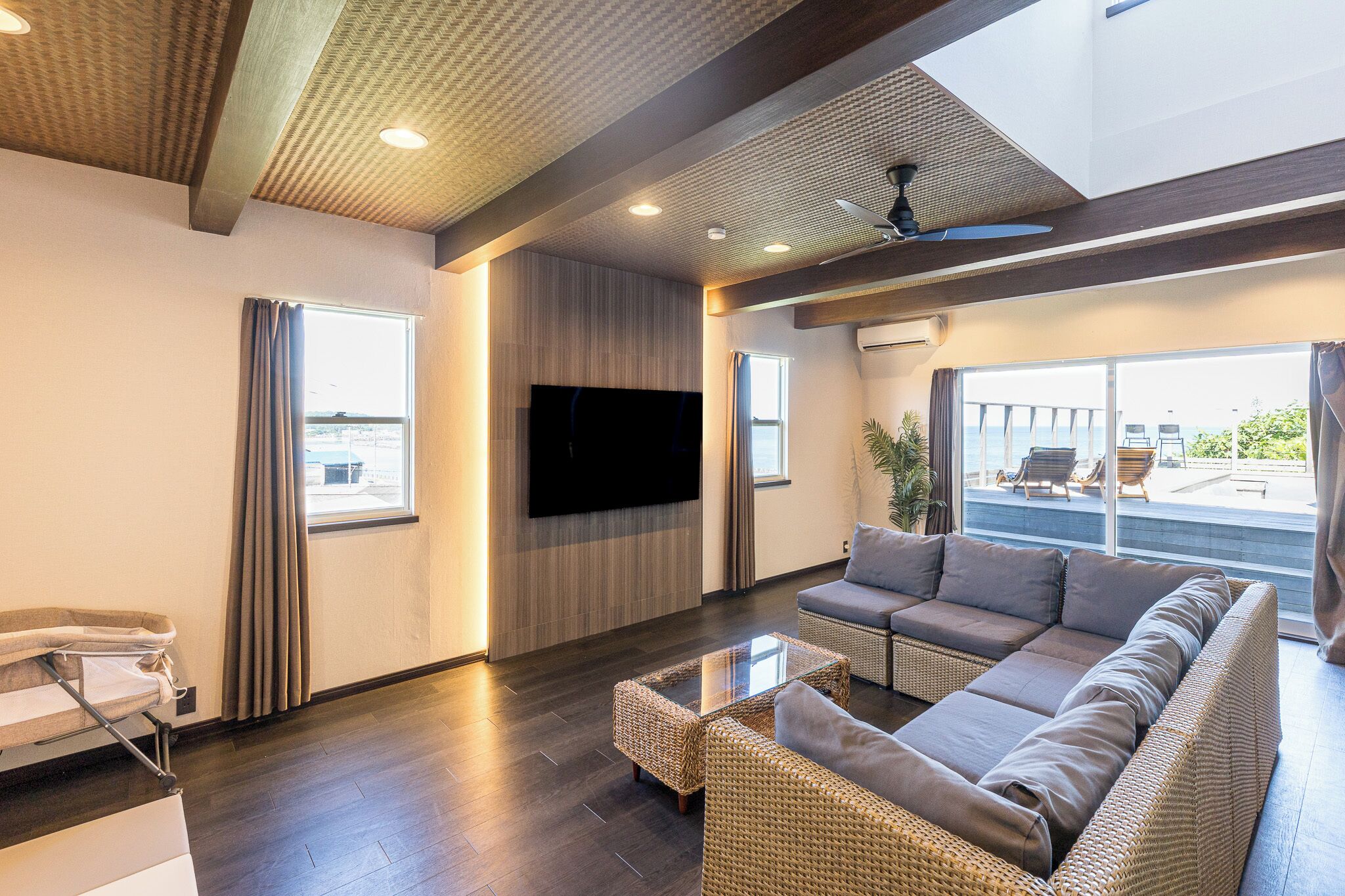 A modern living room with a large sofa, a flat-screen TV, and a ceiling fan.