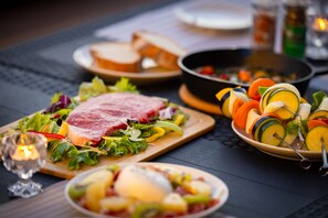Una mesa de comedor con varios platos, entre ellos una ensalada, vegetales cortados y un guiso de carne.