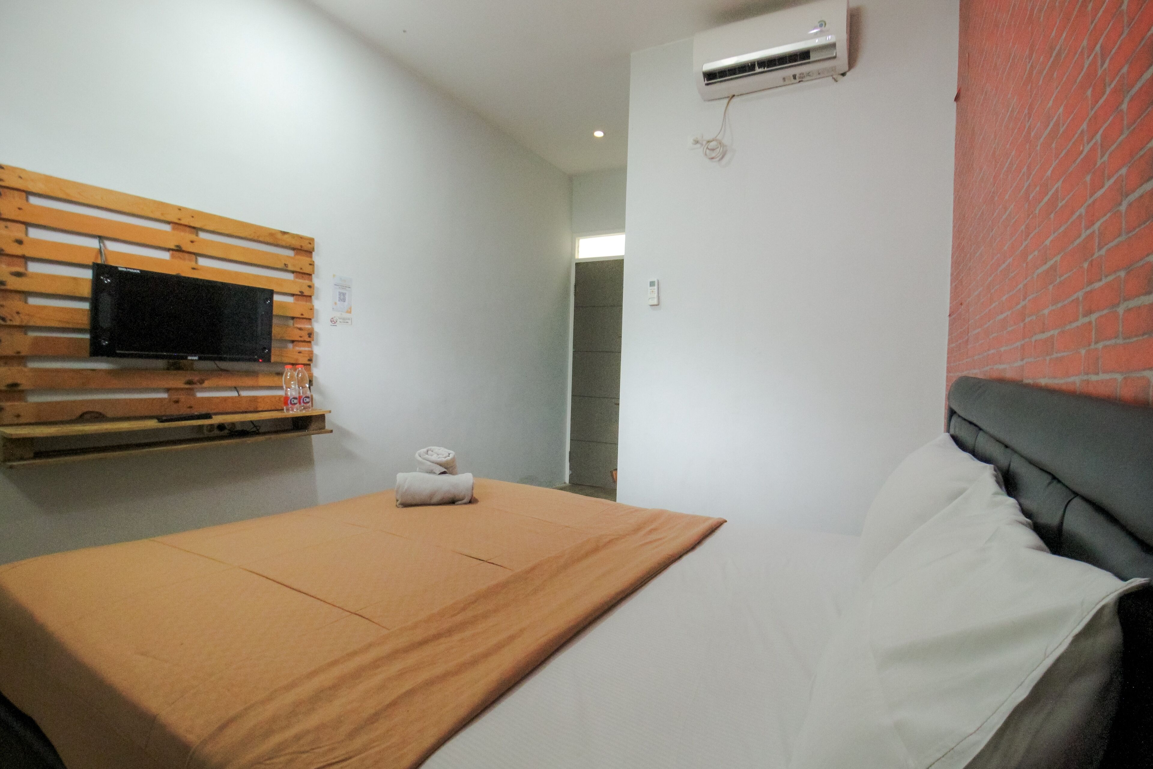 Ein Hotelzimmer mit Bett, einem an der Wand befestigten Fernseher, einer Klimaanlage und einer Ziegelwand.