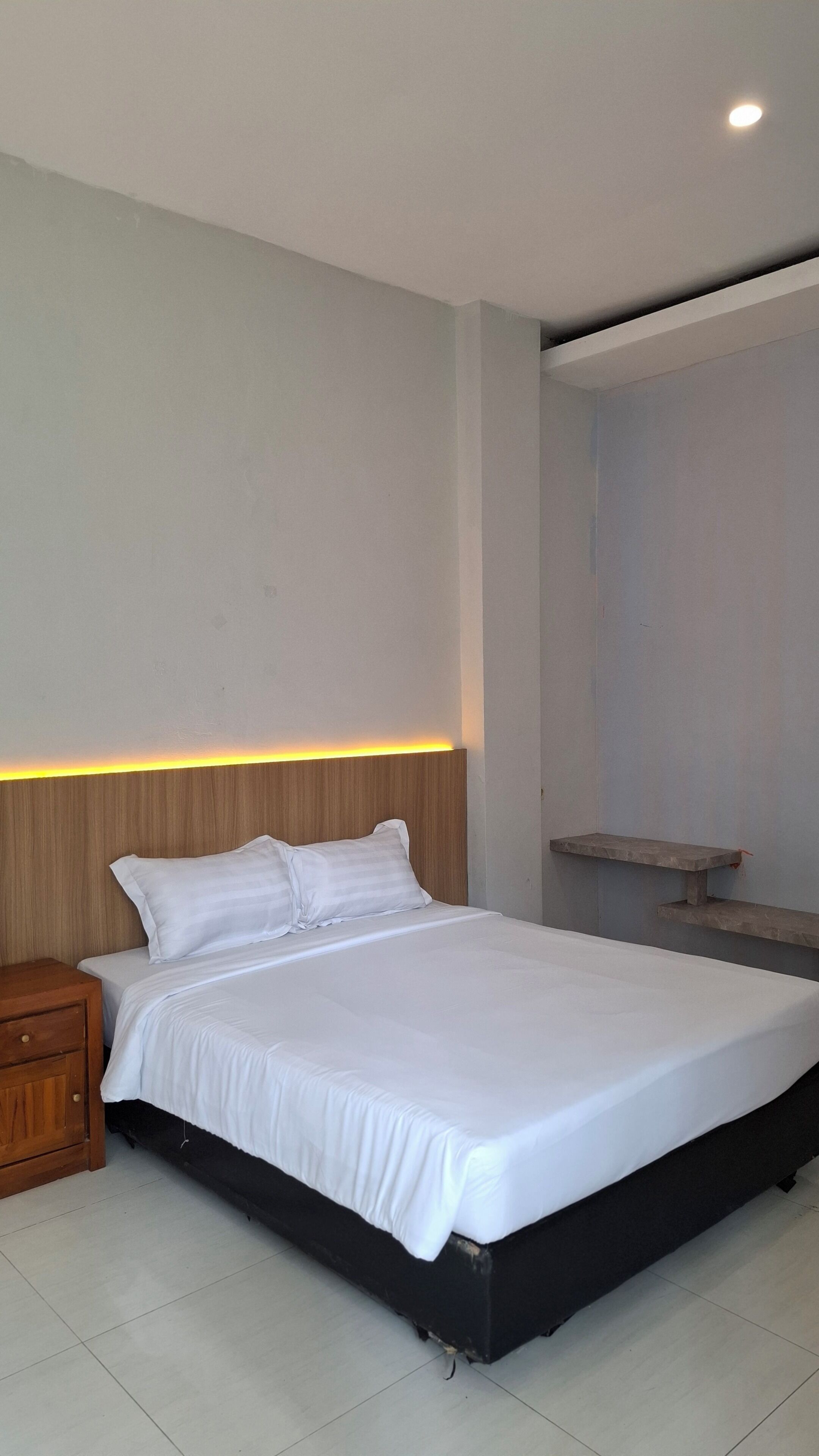 Quarto moderno com cama, mesa de cabeceira e cabeceira de madeira com iluminação embutida.