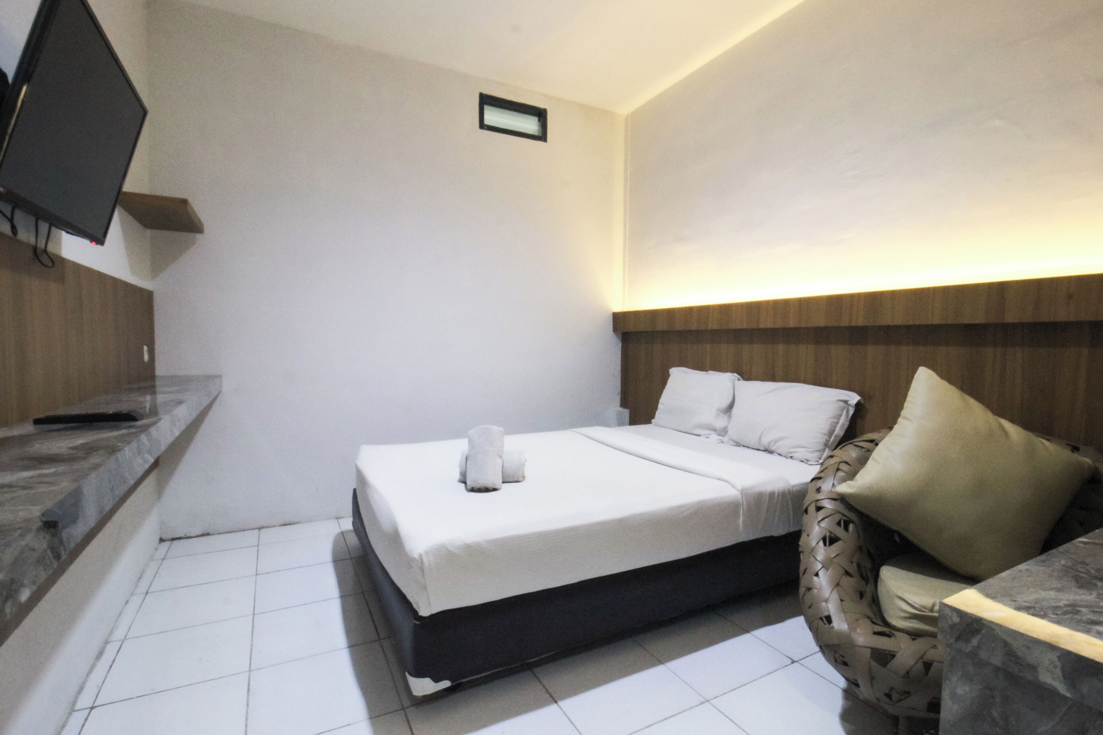 A hotel room with a bed, a TV mounted on the wall, a small bedside table, and a chair with a cushion.