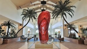 Un vestíbulo amplio con una escultura roja central, palmeras y zonas de estar.