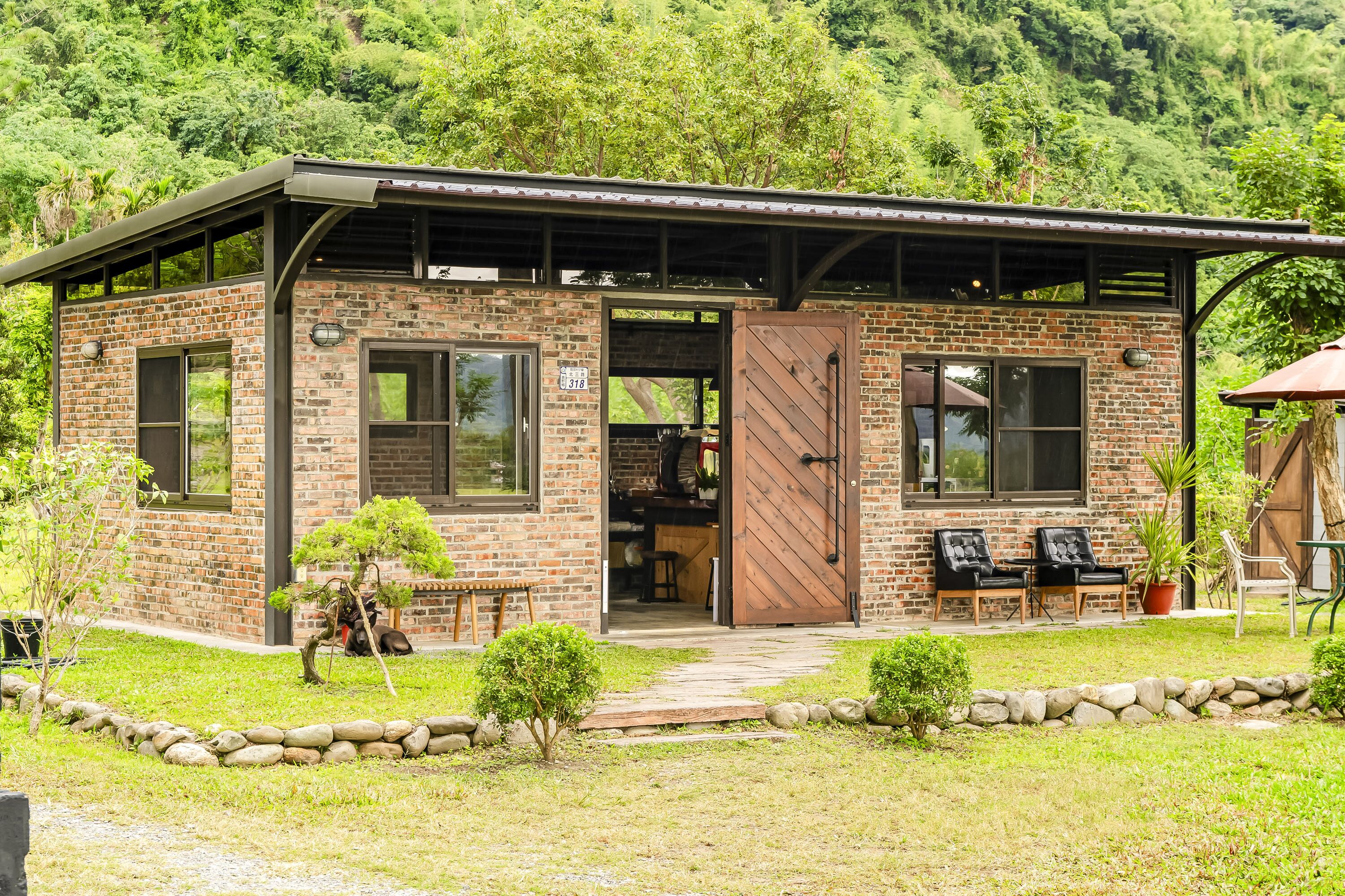 A brick building with a covered porch, a door, and a small garden area with a pathway.