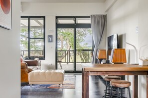 A modern living room with a large sliding glass door leading to a balcony, a wooden dining table with stools, and a comfortable sofa. - Dream Field (Luye)