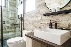 Un baño moderno con cabina de ducha de vidrio, inodoro blanco y un lavabo grande con encimera de mármol.