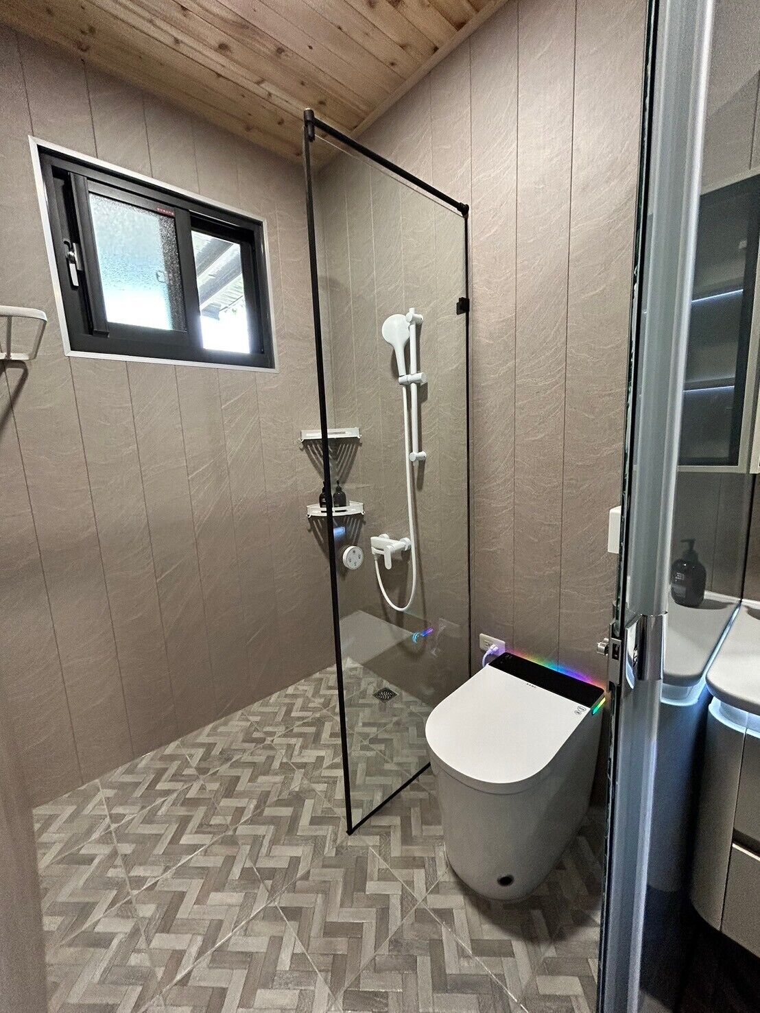 A modern bathroom with a glass-enclosed shower, a white toilet, and a herringbone-patterned floor.