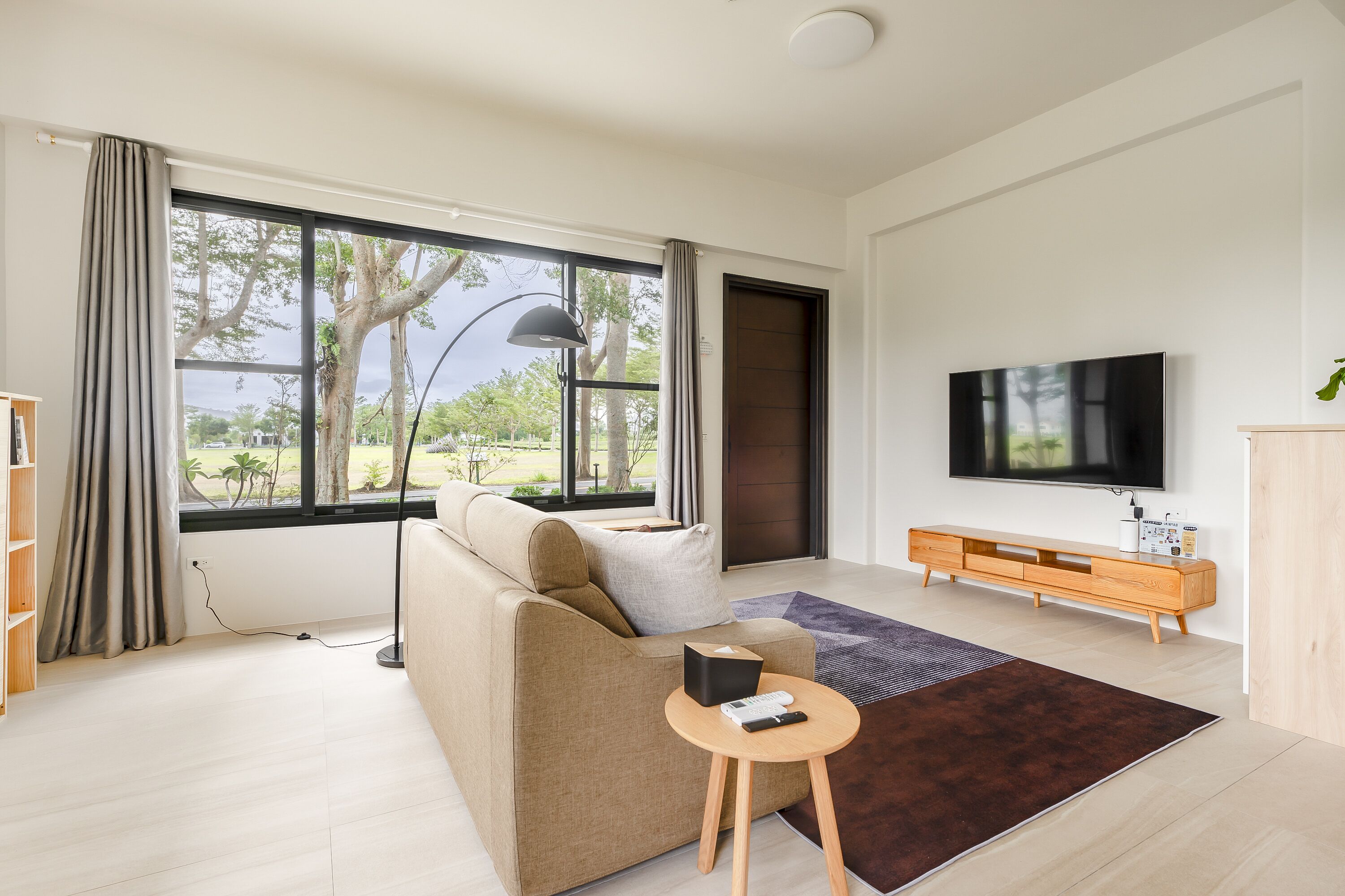 A modern living room with a sofa, a coffee table, a TV, and a large window with a view of trees.