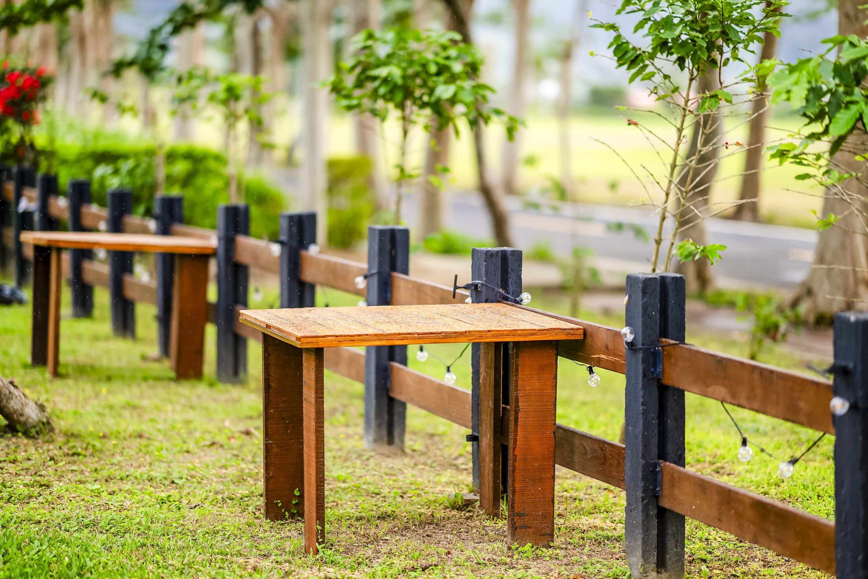 Een houten tafel met metalen frame, ondersteund door een houten omheining met zwarte palen en lampen aan de palen bevestigd.