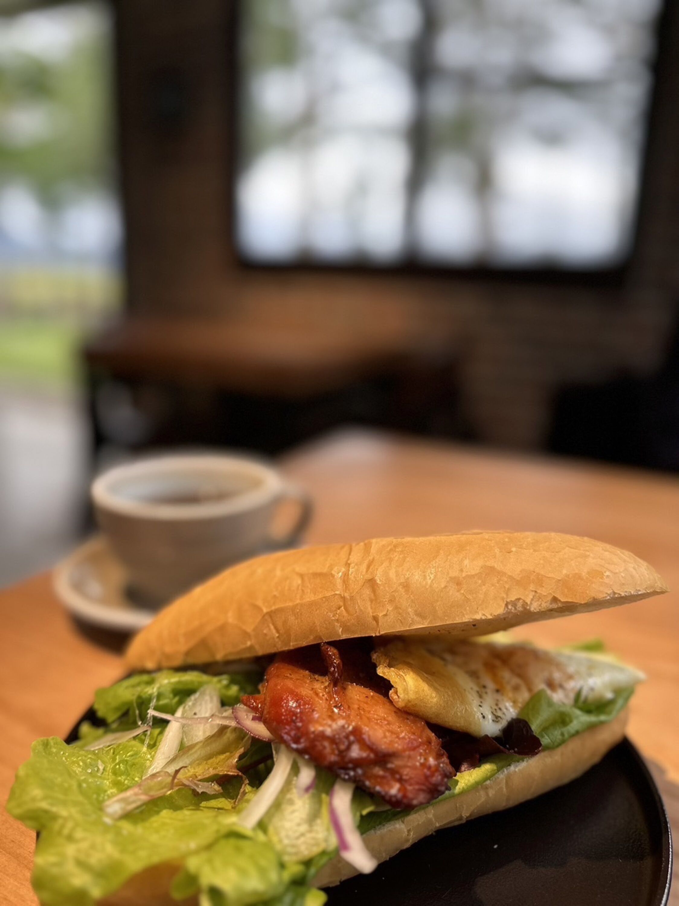 Un sándwich sobre un plato negro, con una taza de café al fondo.