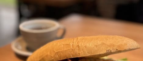 Un sándwich sobre un plato negro, con una taza de café al fondo.