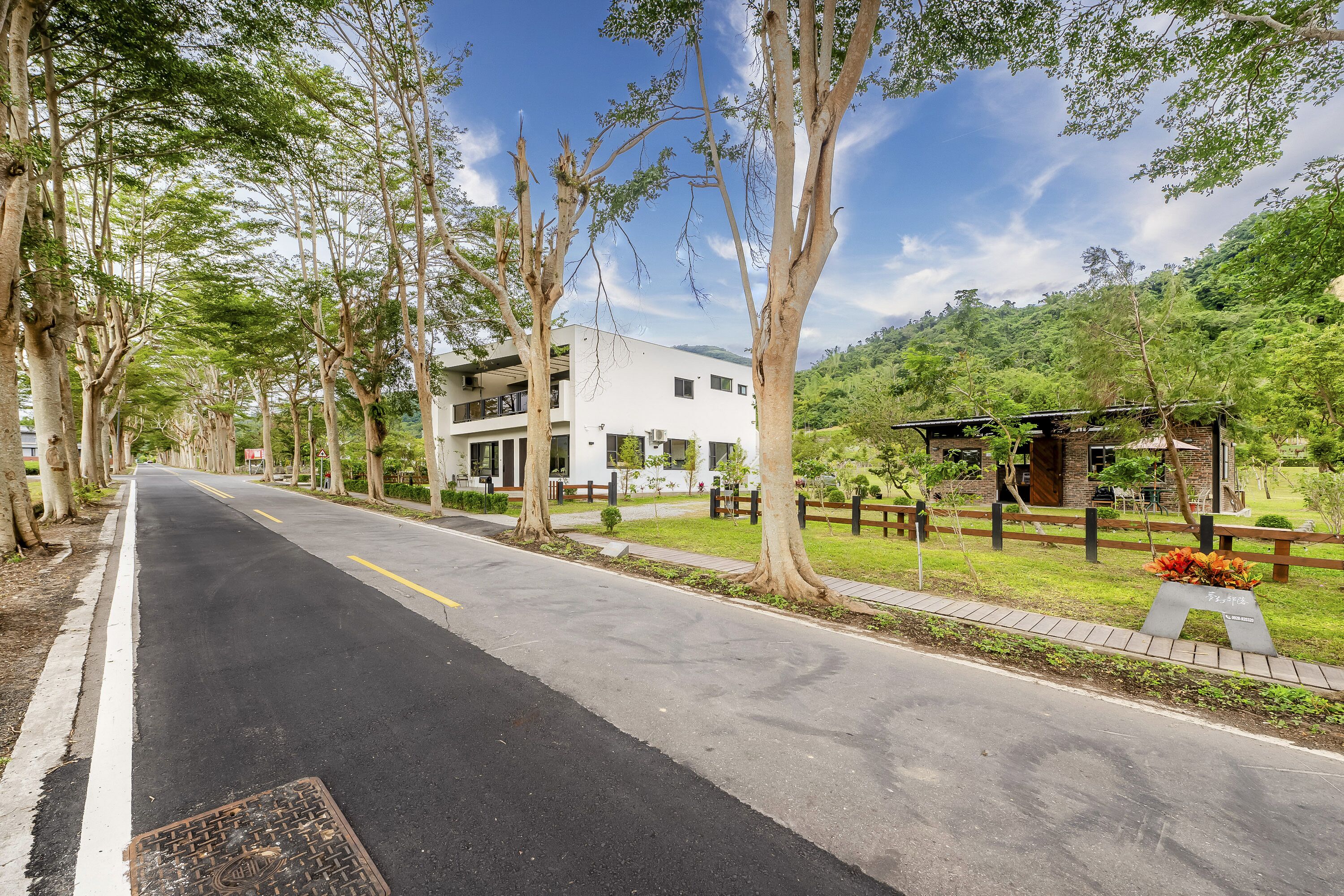Une rue bordée d’arbres, avec un bâtiment moderne, un trottoir et un petit espace vert aménagé en parc.
