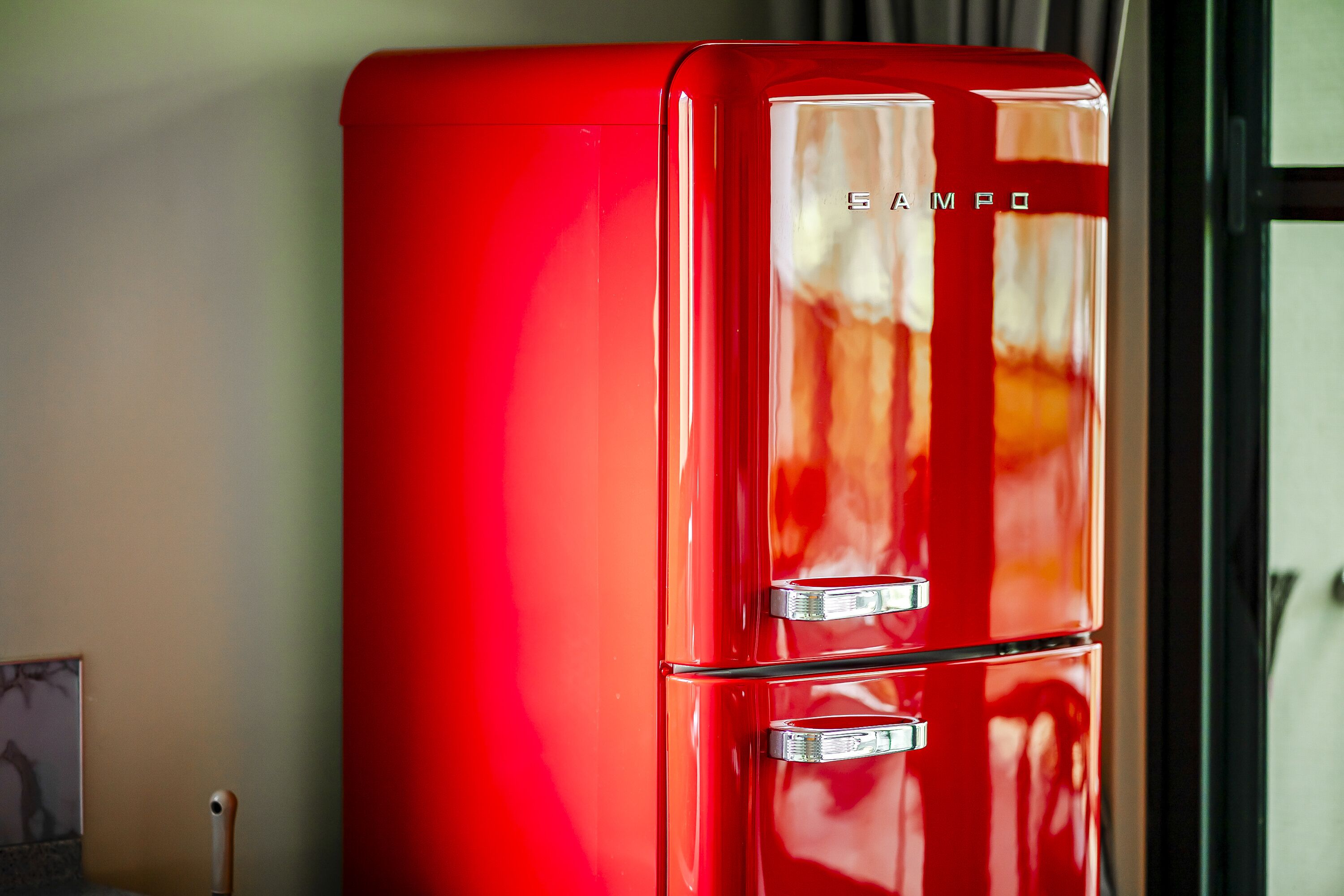 Un réfrigérateur rouge à deux portes, avec le nom de la marque « SAMPO » inscrit sur la porte du haut.