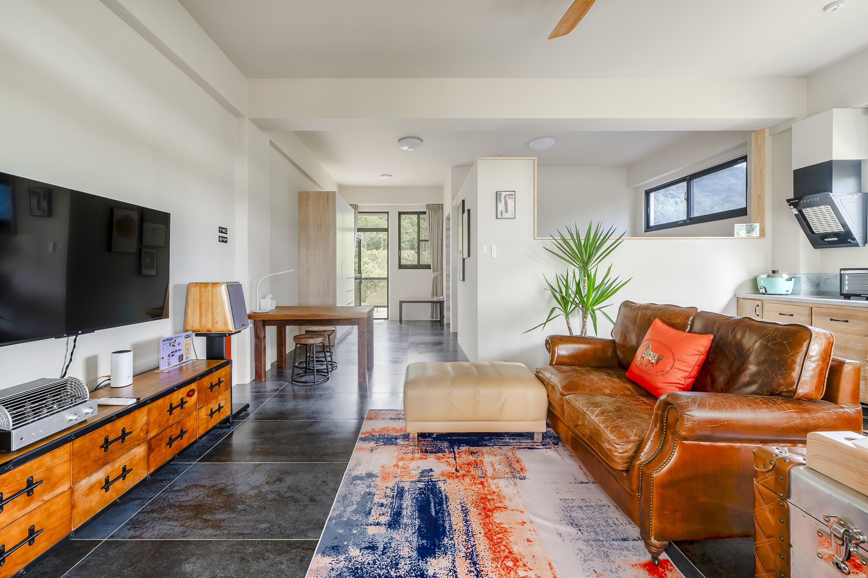 A modern living room with a leather sofa, a TV, and a dining area with a table and chairs.
