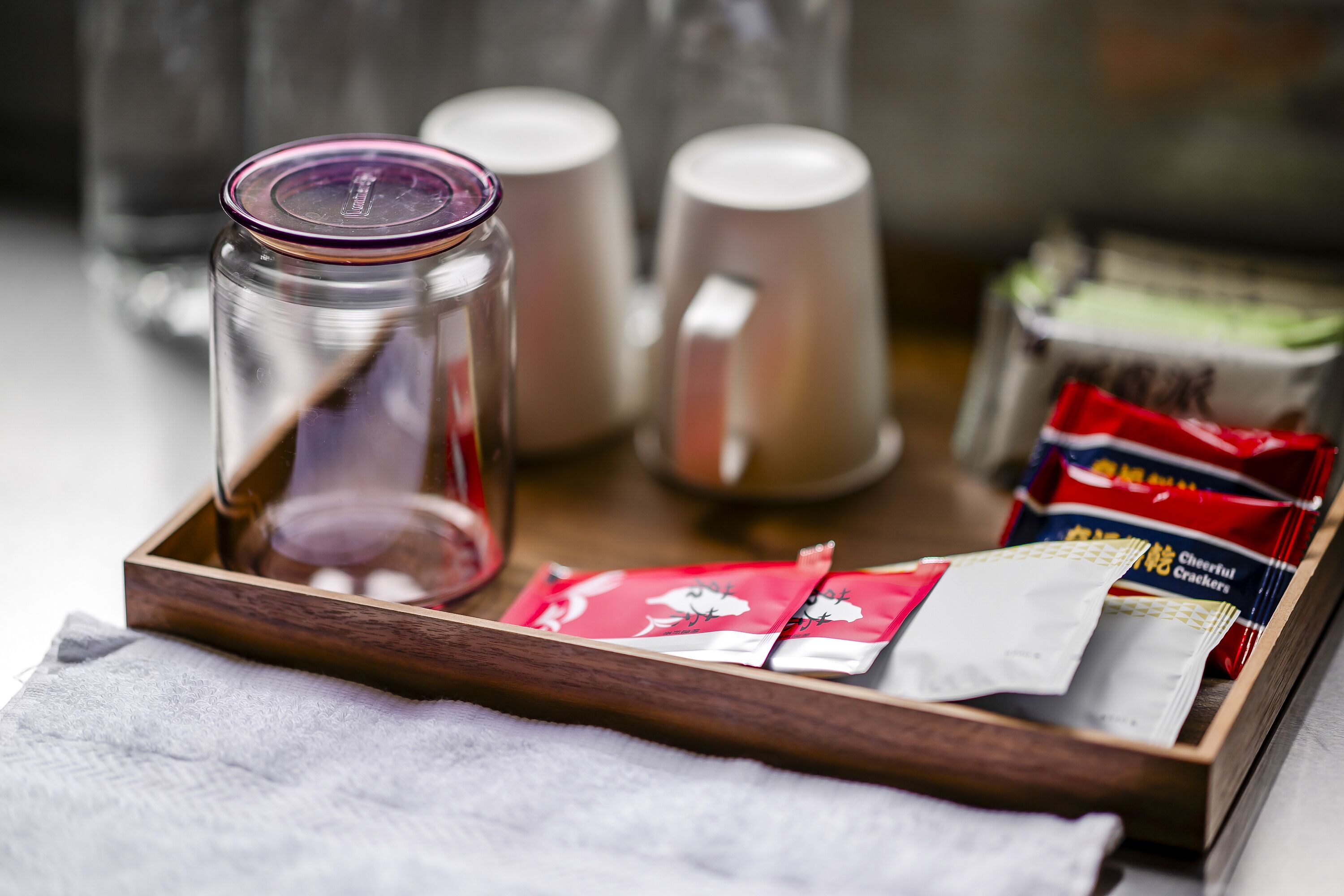 A tray with a glass jar, two mugs, and packets of crackers.