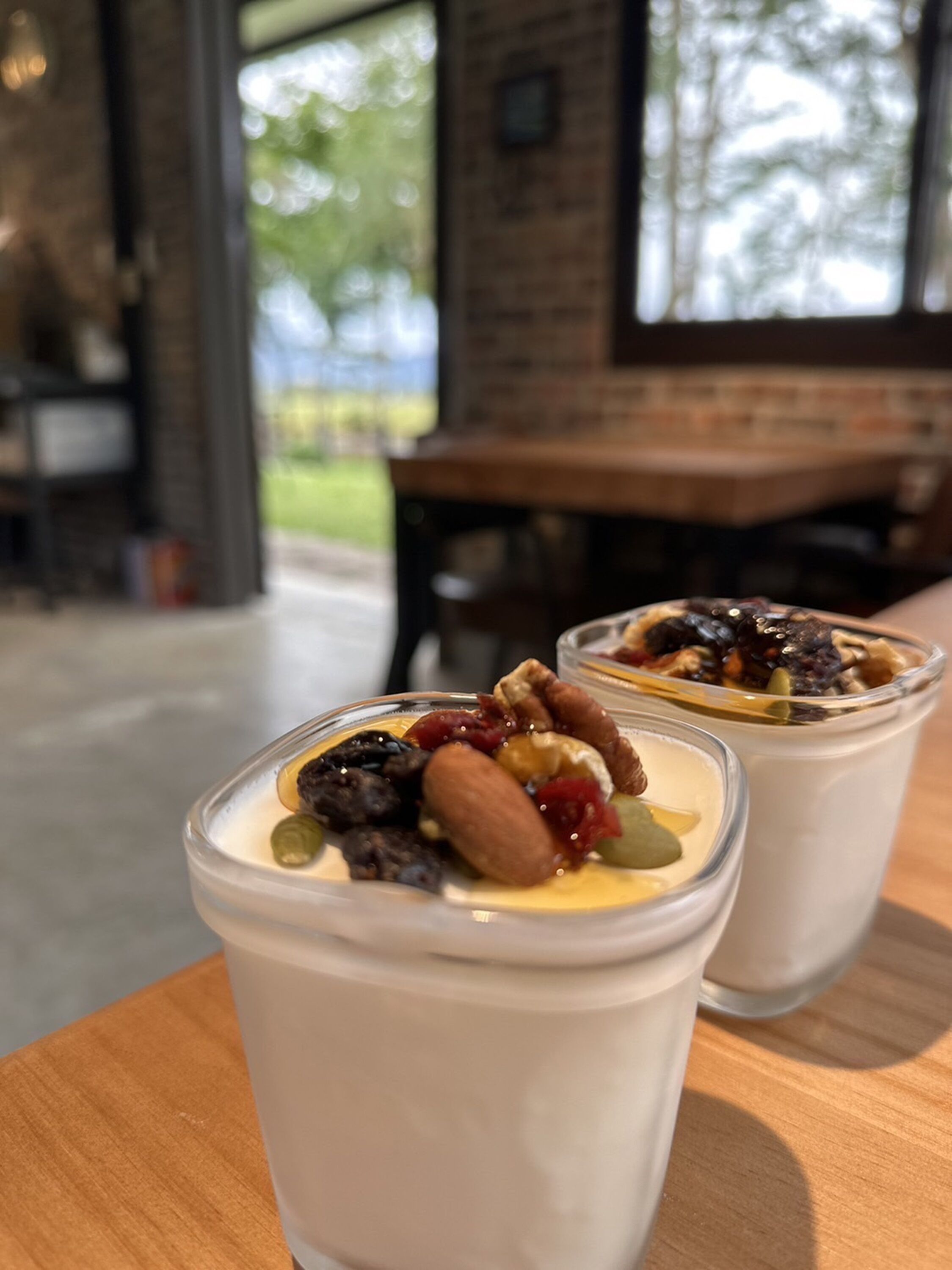 Deux coupes de dessert, garnies de noix et de fruits secs, sont posées sur une table en bois dans un café dont les murs sont en briques et qui possède de grandes fenêtres.