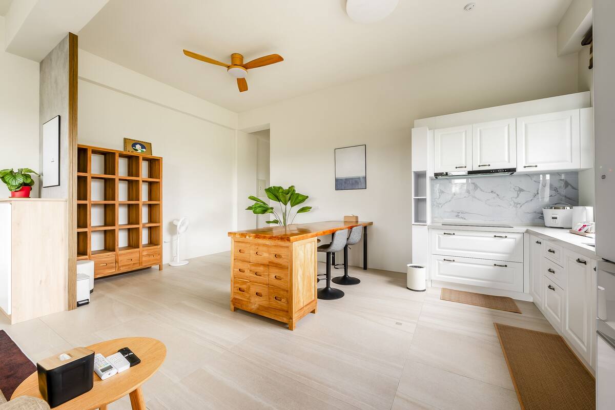 Cozinha moderna com armários brancos, ilha de madeira e ventilador de teto.