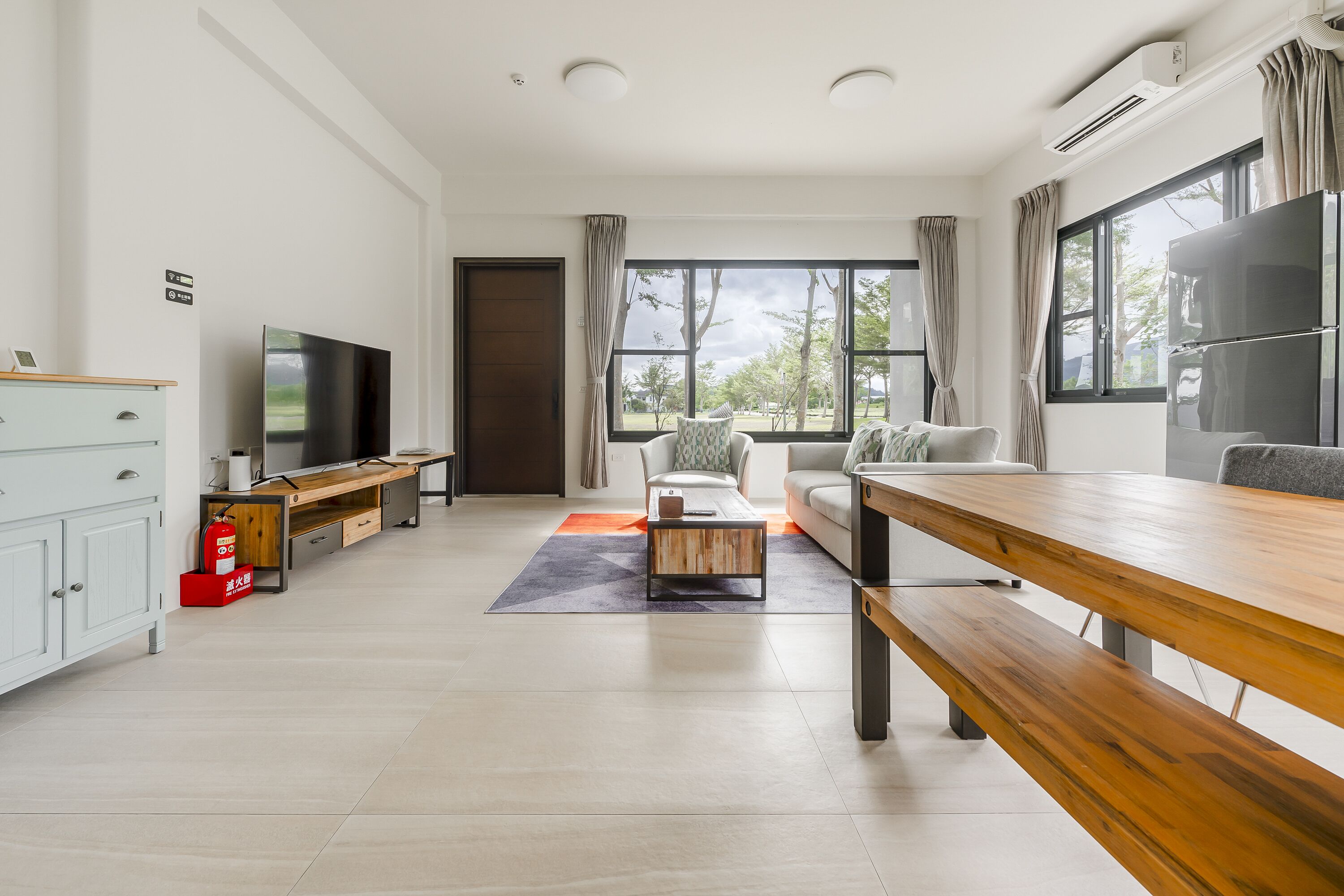 A modern living room with a sofa, coffee table, and TV. There is a wooden bench and a small table with a fire extinguisher.