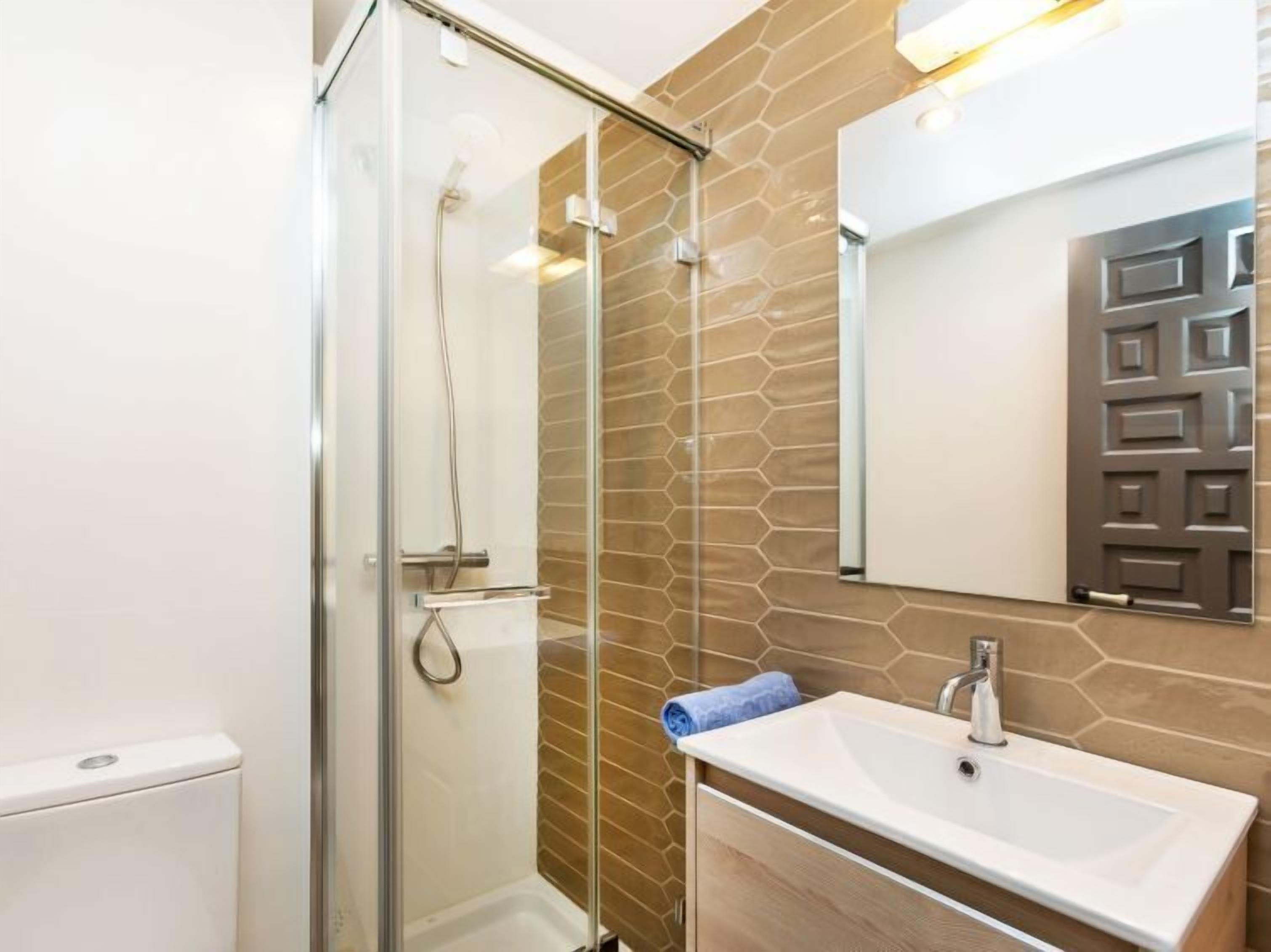 A modern bathroom with a glass shower enclosure, a white sink, and a mirror with a geometric design.