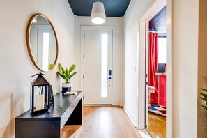 Un couloir avec un miroir, une plante en pot, un bureau avec une lampe et une porte donnant sur une autre pièce.
