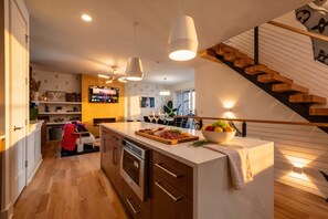 A modern kitchen with a central island, wooden staircase, and a dining area with a TV.