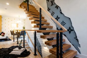 A modern staircase with wooden steps and metal railings, leading to a dining area with a table and chairs.