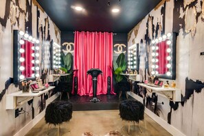 A salon with vanity mirrors, makeup brushes, and a red curtain.
