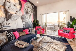 Ein Wohnzimmer mit einer schwarzen Couch, roten Sesseln, einem Glastisch und einem großen Wandbild.