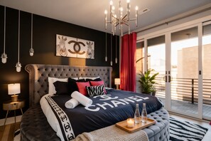A modern bedroom with a large bed, a chandelier, a red curtain, and a balcony with a view.