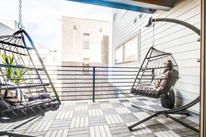 A balcony with two hanging chairs, a wooden floor, and a view of a building in the background.