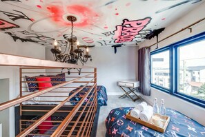 A room with bunk beds, a chandelier, a desk, and a window with a city view.