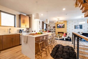 A modern kitchen with wooden cabinets, a central island with bar stools, and a dining area with a fireplace.