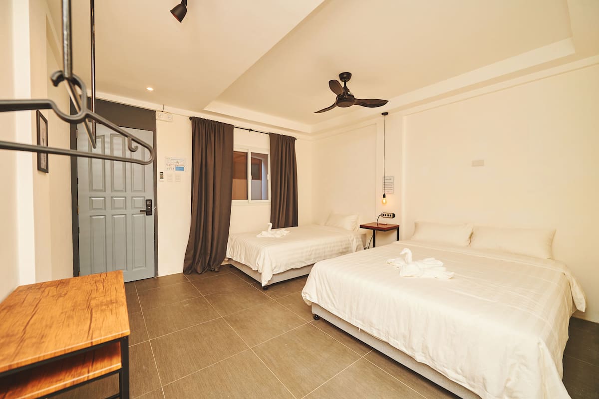 A hotel room with two beds, a wooden table, a ceiling fan, and a door.