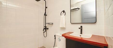 A bathroom with a toilet, sink, mirror, and shower.