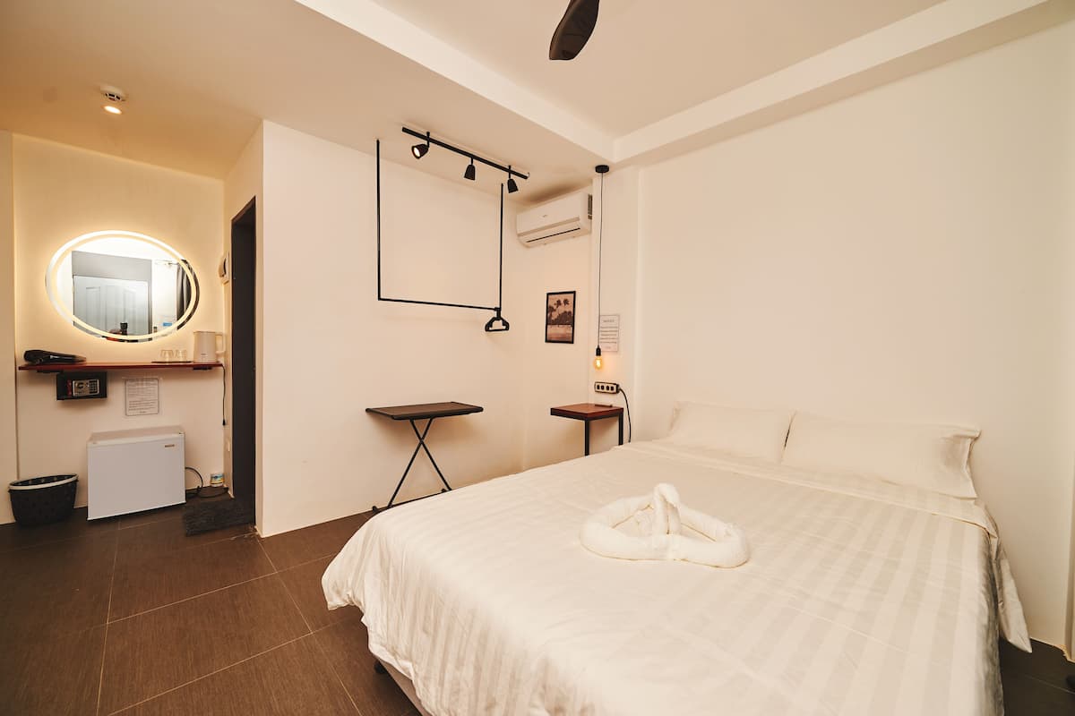 A hotel room with a large bed, a round mirror, a small table, a heater, and a wall-mounted air conditioner.