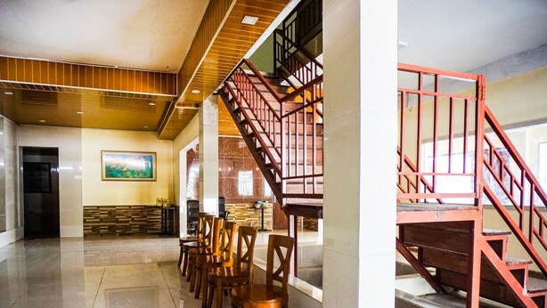 A spacious lobby with a long row of wooden chairs, a staircase with red railings, and a painting on the wall. - OYO 93066 D'niel Homestay Syariah (Medan)