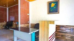 A reception desk with a glass top and teal legs, a wooden counter with a red stripe, and a framed abstract painting on the wall. - OYO 93066 D'niel Homestay Syariah (Medan)