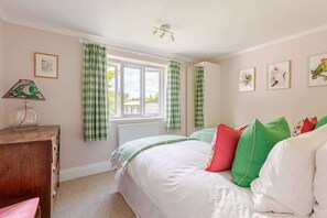 Un dormitorio con cama, cómoda, ventana con cortinas e imágenes enmarcadas en la pared.