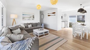 Ein modernes Wohnzimmer mit einem grauen Sofa, einem weißen Couchtisch und einem Essbereich mit weißen Stühlen und einem Tisch.